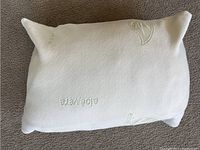 White pillow with aloe vera embossed text and leaf patterns, shown from one angled side.