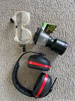 Radians ear muffs placed on carpet, accompanied by clear protective goggles and Silencer headset light.