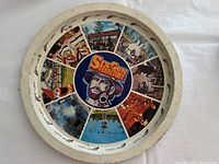 Top view of the round metal tray showing colorful Sixgun Territory themed illustrations divided into 13 sections around a central cowboy figure. The tray background is white with some paint loss visible.