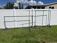 Photo showing three metal clothing racks of different designs and sizes outside on grass against a white fence.