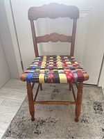 Front view of antique wooden chair showing carved backrest and woven fabric seat made from multicolored fabric strips.