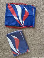 Two British Airways branded drawstring backpacks laid flat on carpet. One sealed in original packaging, the other opened but unused.