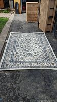 Area rug displayed on driveway with clear view of floral pattern and border design.