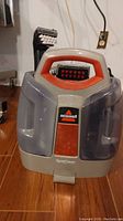 Front view of the Bissell SpotClean portable carpet cleaner showing the transparent water tanks, handle, and front label.