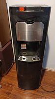 Front view of black bottom mount water dispenser with silver dispensing area and orange switch on top front.