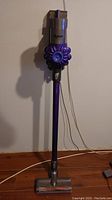 Full upright view of Dyson V6+ on hardwood floor showing stick, floor head and wall mount bracket.