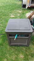 Closed dark brown textured plastic hose storage box with an attached green garden hose visible through the outlet.