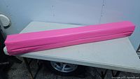 Gymnastic balance beam folded and fully padded in pink, showing overall exterior condition on folding table.