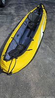 Photo showing yellow and gray Tobin Sports inflatable kayak inflated and set on pavement with adjustable seat inside