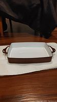 Front view of Dansk Kobenstyle roasting pan baker showing rectangular shape, white enamel interior, chocolate brown exterior and two handles.