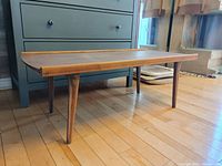 Side view of the wooden coffee table showing tapered legs and raised edge detail.