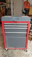 Front view of the metal tool box showing red frame with four gray drawers including one cubby drawer and wheels.