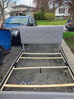 Queen size gray upholstered bed frame showing headboard with button tufting and wooden slats inside metal frame rails.