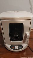 Front view of white vertical rotisserie oven with closed glass door and control knob on the front base.