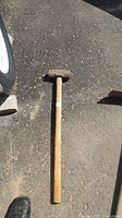 Full view of a heavy sledge hammer lying on the ground showing wooden handle and metal head.