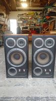 Front view of the two Wharfedale E.Fifty speakers showing their speaker cones and controls on a concrete floor in a workshop environment.