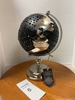 Full view of the modern black metal globe with silver continents on a silver stand, showing the perforated design and overall shape.