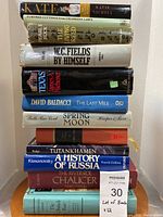 Photo shows 12 used books stacked vertically with titles and authors visible. Condition shows some wear.