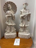 Pair of ceramic sculptures, male and female figures, with detailed traditional clothing and accessories, standing on decorated bases.
