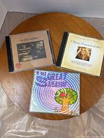 Three CD jewel cases showing cover art for Jim Jelly Godfrey, Olivia Newton-John, and The Great Sabrina albums on a round table.
