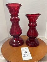Front view of two red glass vases on a wooden base, showing their individual shapes and polished red glass surface.