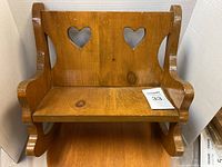 Front view of a wooden doll bench showing heart shaped cut outs on the backrest and curved armrests.