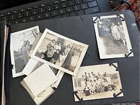 Photo of several vintage black and white photographs collected loose and mounted on black album pages, showing families and groups outside.
