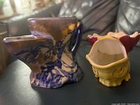 Two antique personal tea strainer pitchers side by side on black leather surface, yellow smaller pitcher with spout and some chip visible, larger blue and white china pitcher with floral pattern.