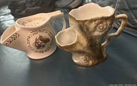 Two antique personal tea strainer pitchers shown side by side on dark surface, white with horse decal and naturalistic textured brown pitcher