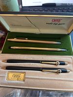 Photo showing both pen sets inside their original boxes with soft fabric lining, one black set with gold accents and one gold-colored set