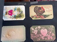 Four vintage postcards in black album page: Thanksgiving turkey card, a woman in pink, embossed floral card, and a card with heart and flowers saying 'Forget Me Not'.