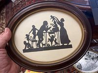 Oval framed silhouette artwork showing a family with child and toys in black against cream background.
