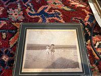 Photo of framed cabinet photograph showing two children standing in shallow water or wet sand at a beach or shoreline.