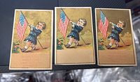 Three Victorian trade cards showing a child holding an American flag in blue attire on gold background, all slightly worn.