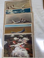 Five stacked color prints showing different Lockheed airplanes in flight, with one print visible in detail having a white airplane with red accents and US Navy insignia above clouds and rugged terrain.