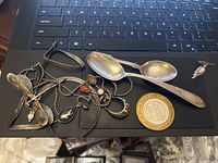 Overview of lot jewelry, spoons, poker chip, and earrings on laptop keyboard