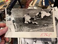 Black and white action photo of early Atlanta Braves player sliding into base with catcher and umpire nearby.