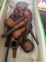 Box containing about ten vintage briar smoking pipes with varying shapes and stem conditions.