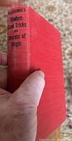 Red hardcover book cover with title printed on spine held in hand