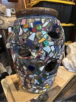 View of mosaic planter showing multicolored tiles, glass pieces, a green die attached near the eye hole, and a watch piece embedded in the design.