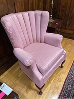 Front left angle view of the pink upholstered armchair showing scalloped vertical channel backrest, rolled arms, and wooden cabriole legs