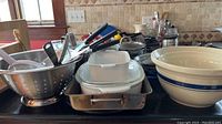 Overall view of lot showing metal strainer, roasting pan, stoneware mixing bowls, Pyrex lidded bowl, Corning Ware dish, and various utensils on countertop