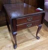 Side view of wooden drop leaf side table showing two drawers and cabriole legs, with a polished finish.