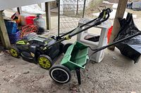 Ryobi cordless lawn mower in black and yellow with foldable handle and cord storage on the handle, four wheels.