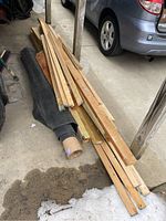 Pile of assorted scrap lumber and rolled black rubber or vinyl sheet next to a car.
