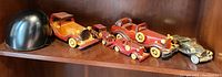 Shelf display of 4 wooden classic car model figurines in shades of brown and a metal classic car model, along with a black helmet-shaped item.