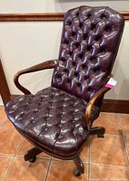 View of chair angled to show tufted upholstery, wooden armrests, and base castors.