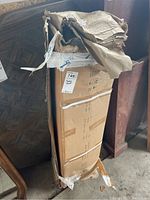 Photo of tall cardboard box with multiple tape straps containing the party tent, box top damaged and bent.