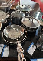Multiple pots and pans stacked showing variety of sizes and lids with some cookware showing signs of use and dirt.