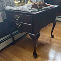 Side view of dark wood one-drawer side table with glass top, showing table leg detail and brass handles on the drawer.